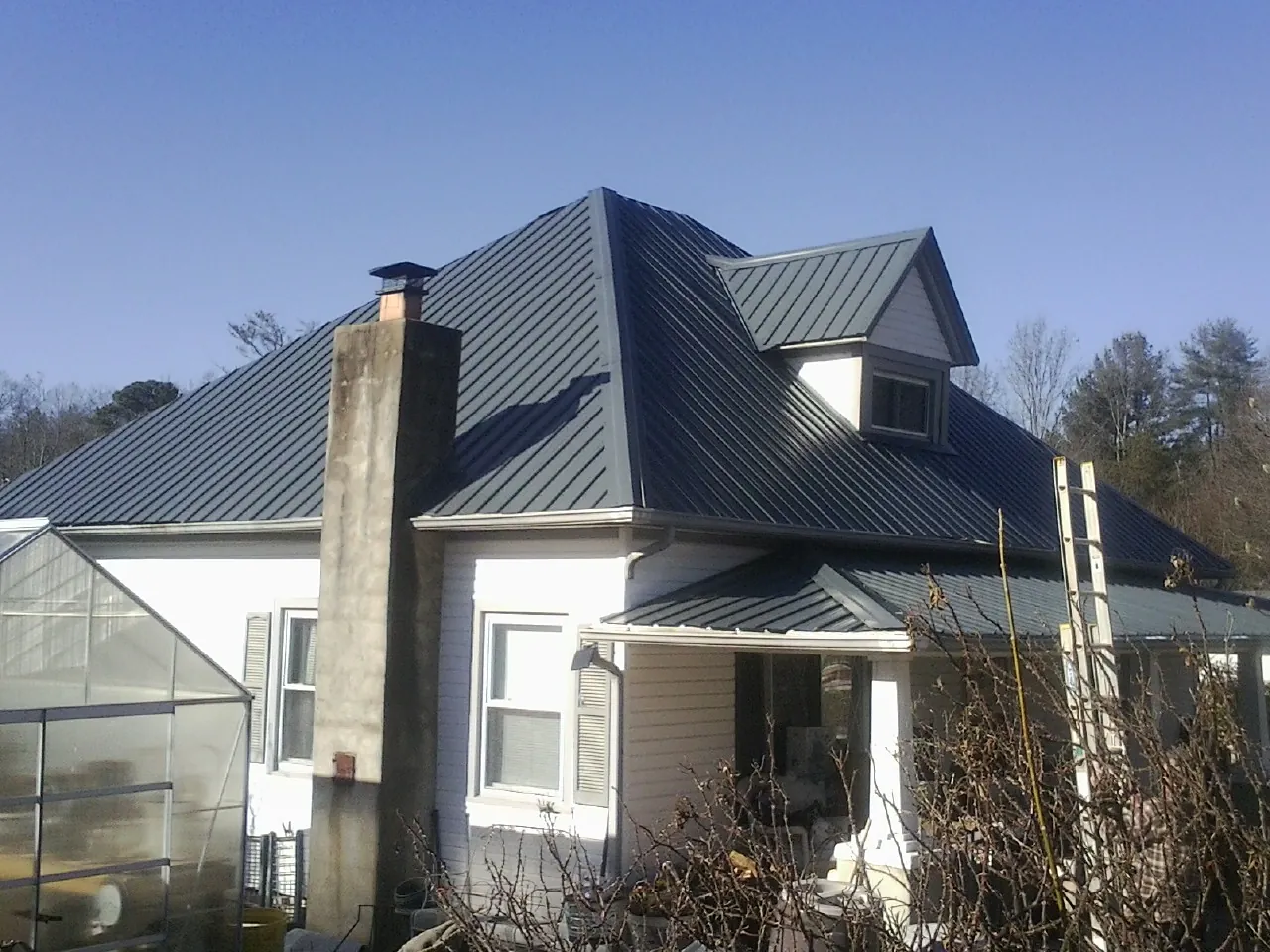 Dark blue standing seam metal roof on a white farmhouse with dormer — Slate & Tile Roof Repair by Roofing Brothers in Dexter