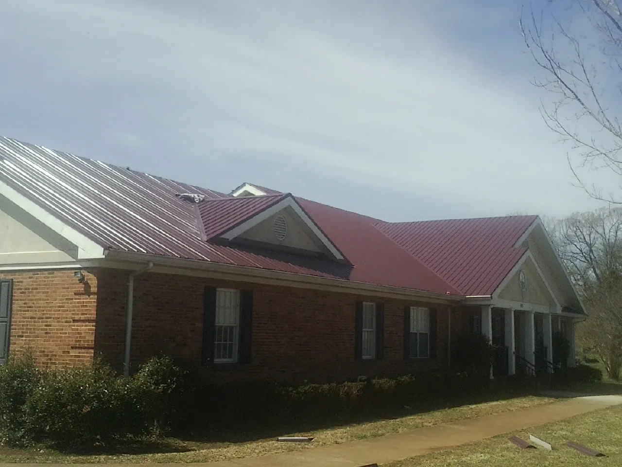 Red metal roof with gabled entries on a long brick building, from a Hail Damage Roof Repair job in Dexter