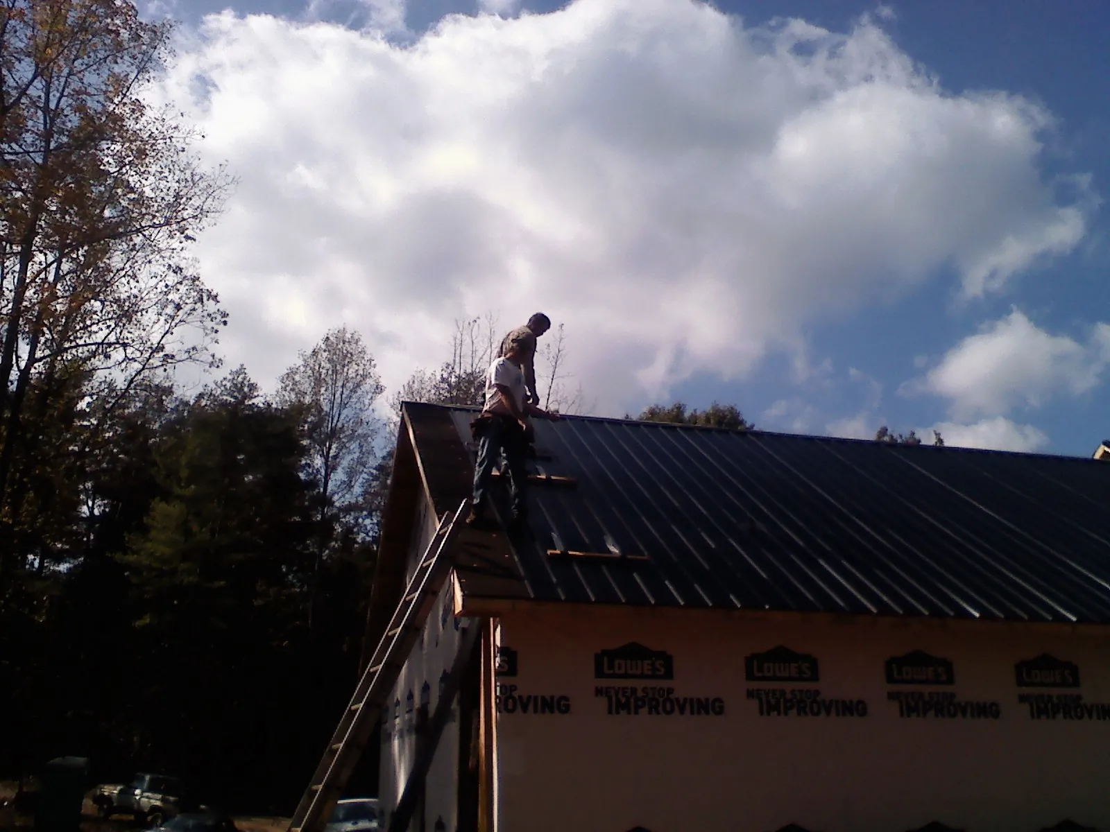 Roofer fastening dark metal panels high against a cloudy sky, from a Roof Inspection job in Dexter